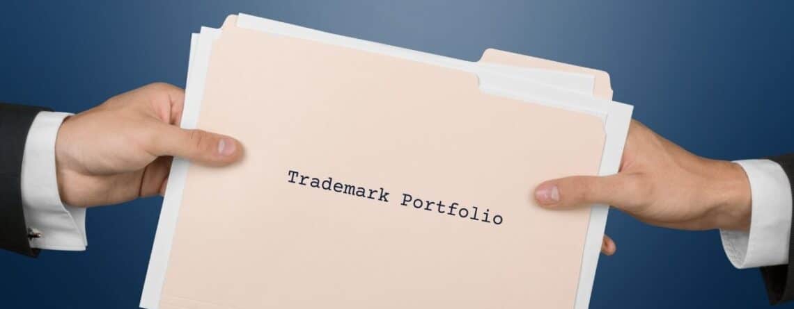 Two hands exchanging a beige folder labeled 'Trademark Portfolio' beneath a banner that reads 'IP Decisions'